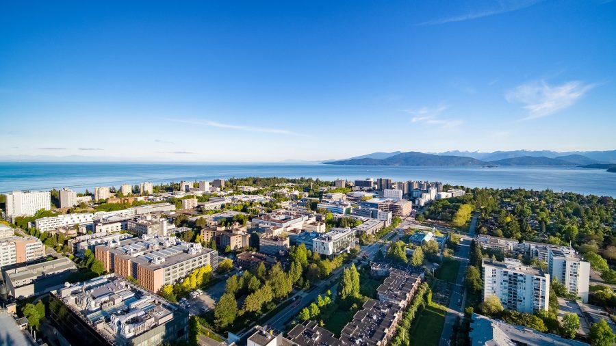 A wide cityscape under a clear blue sky with the ocean visible in the distance, capturing the vibrant environment surrounding the University of British Columbia.